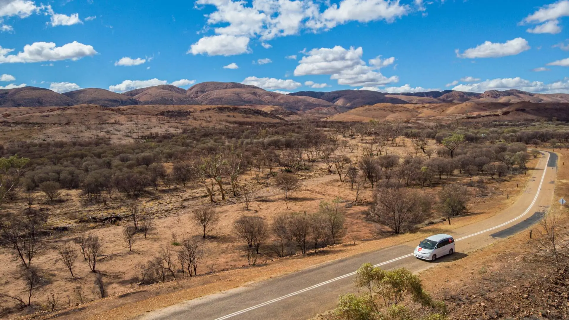 Spaceships campervan exploring Australia - rugged nature in the distance while campervan drives through it on macadam road